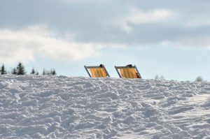 Zwei Liegestühle auf verschneitem Boden vor einer winterlichen Landschaft.