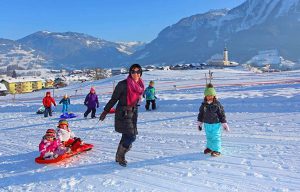 Familie beim Rodeln im schneebedeckten St. Veit im Pongau mit Alpenpanorama im Hintergrund.
