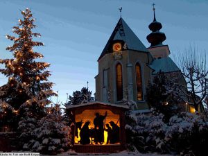 Weihnachtliche Szene mit erleuchteter Kirche und verschneitem Baum in St. Veit im Pongau.